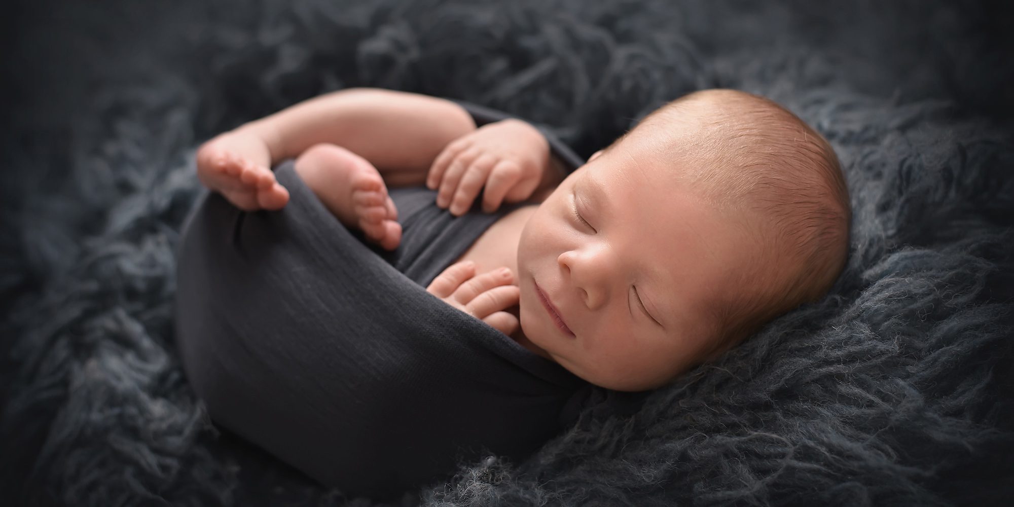 newborn boy wrapped in dark blue