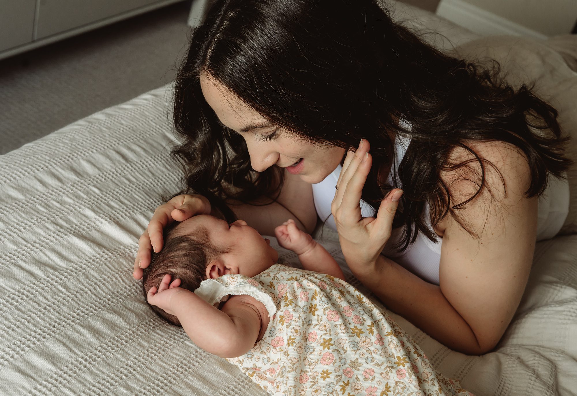Mother looking at her newborn in her bedroom during a lifestyle photography session in Hamilton